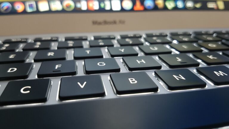 Teclado de MacBook com teclas de volume destacadas ao lado de um monitor LG mostrando ondas de som