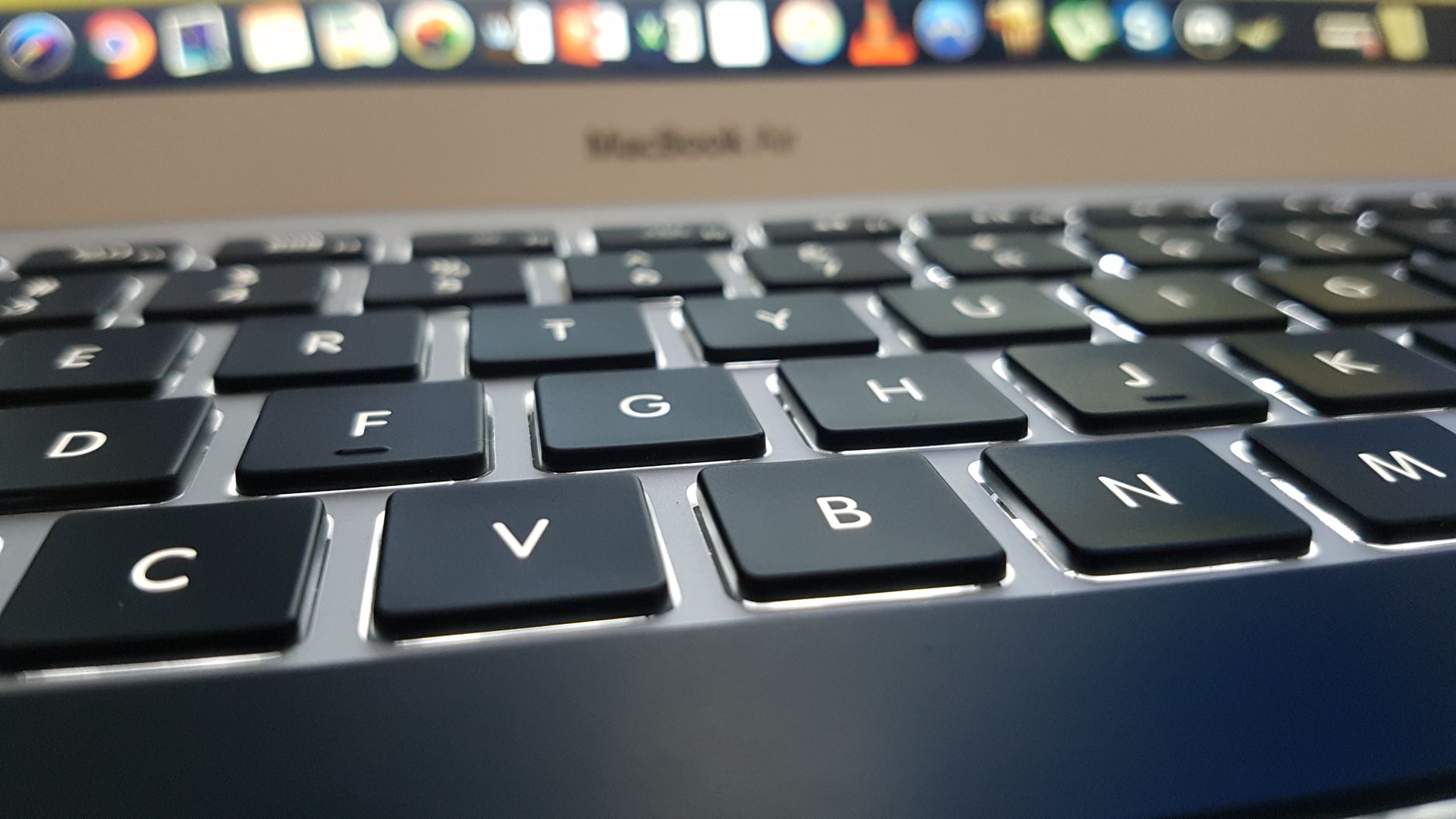 Teclado de MacBook com teclas de volume destacadas ao lado de um monitor LG mostrando ondas de som